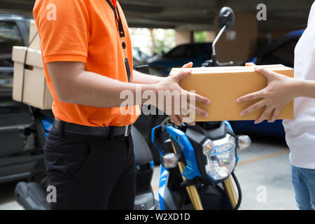 Donna mano accetta una consegna di scatole da deliveryman, consegnare merci in motocicletta, servizio veloce e trasporto gratuito Foto Stock