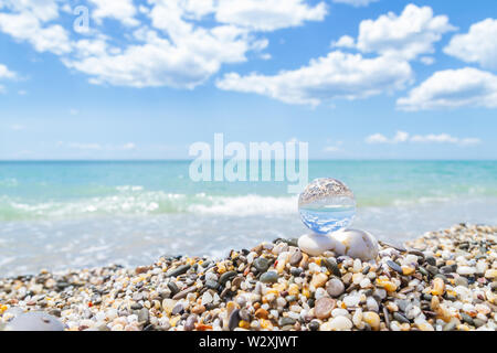 Vetro sfera tonda sulla spiaggia riflette il mare in estate Foto Stock