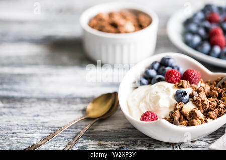 Lo yogurt greco, mirtilli e lamponi e granola in una ciotola bianco su uno sfondo di legno. Foto Stock