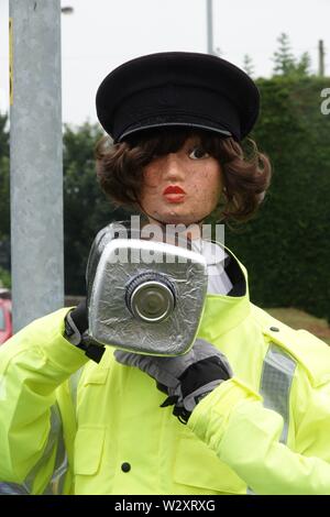 Sefton, Merseyside, Regno Unito. 11 luglio 2019. Poliziotta armata con fotocamera velocità provoca il passaggio agli automobilisti in Southport Rd, Sefton a lento in giù non appena essi scorgere la sua. In realtà il funzionario di polizia è uno spaventapasseri in un alto-vis jacket la velocità fotocamera è realizzato da un vuoto bottiglia di sbianca coperta con un foglio di alluminio. Denominato 'Speedo' è stato creato da 71-anno-vecchio consigliere parrocchiale Edie Papa chi corre in vista della Chiesa Farm Shop in Southport Road, Lydiate, dopo una stringa del traffico su strada gli incidenti causati da persone che guidano per disattenzione o troppo veloce. Credit:Ken Biggs/Alamy Live News Foto Stock