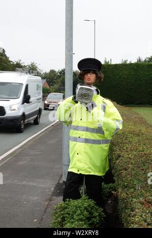 Sefton, Merseyside, Regno Unito. 11 luglio 2019. Poliziotta armata con fotocamera velocità provoca il passaggio agli automobilisti in Southport Rd, Sefton a lento in giù non appena essi scorgere la sua. In realtà il funzionario di polizia è uno spaventapasseri in un alto-vis jacket la velocità fotocamera è realizzato da un vuoto bottiglia di sbianca coperta con un foglio di alluminio. Denominato 'Speedo' è stato creato da 71-anno-vecchio consigliere parrocchiale Edie Papa chi corre in vista della Chiesa Farm Shop in Southport Road, Lydiate, dopo una stringa del traffico su strada gli incidenti causati da persone che guidano per disattenzione o troppo veloce. Credit:Ken Biggs/Alamy Live News Foto Stock