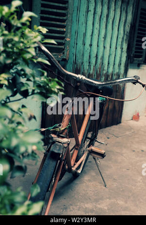 Incredibile close up vecchio anteriore di bicicletta di antica casa, la ruota di bicicletta la ruggine, danneggiata con sfondo sfocato in tono vintage a China Town, Vietnam Foto Stock