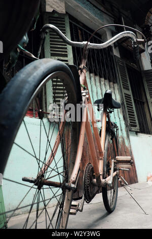 Incredibile close up vecchio anteriore di bicicletta di antica casa, la ruota di bicicletta la ruggine, danneggiata con sfondo sfocato in tono vintage a China Town, Vietnam Foto Stock