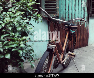 Incredibile close up vecchio anteriore di bicicletta di antica casa, la ruota di bicicletta la ruggine, danneggiata con sfondo sfocato in tono vintage a China Town, Vietnam Foto Stock