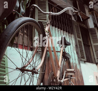 Incredibile close up vecchio anteriore di bicicletta di antica casa, la ruota di bicicletta la ruggine, danneggiata con sfondo sfocato in tono vintage a China Town, Vietnam Foto Stock