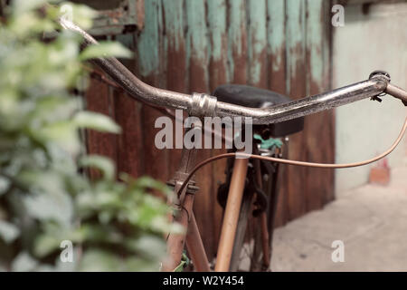 Incredibile close up vecchio anteriore di bicicletta di antica casa, la ruota di bicicletta la ruggine, danneggiata con sfondo sfocato in tono vintage a China Town, Vietnam Foto Stock