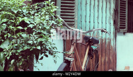 Incredibile close up vecchio anteriore di bicicletta di antica casa, la ruota di bicicletta la ruggine, danneggiata con sfondo sfocato in tono vintage a China Town, Vietnam Foto Stock