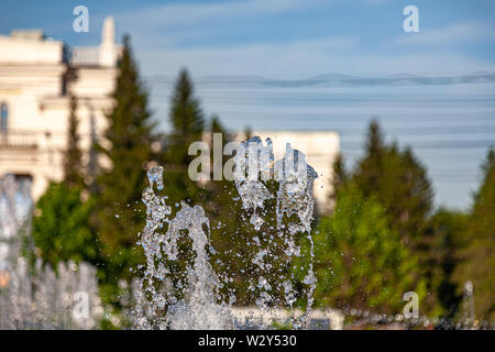 Città fontana con schizzi e getti di acqua contro lo sfondo di edifici e alberi verdi sotto un cielo blu in una limpida giornata estiva Foto Stock