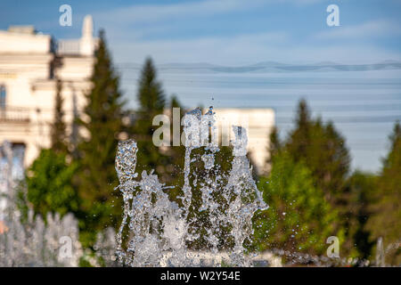 Città fontana con schizzi e getti di acqua contro lo sfondo di edifici e alberi verdi sotto un cielo blu in una limpida giornata estiva Foto Stock