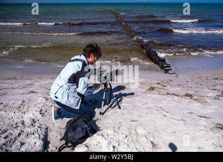 11 luglio 2019, Meclemburgo-Pomerania, Vitte: un giornalista film appena le righe del set di pennelli sulla spiaggia del Mar Baltico isola di Hiddensee. Sulla costa fuori del villaggio di Vitte, un nuovo sistema groyne fu costruito per circa cinque milioni di euro per proteggere efficacemente i villaggi dalle forti mareggiate con un livello di piena fino a 2,60 metri. Foto: Jens Büttner/dpa-Zentralbild/dpa Foto Stock