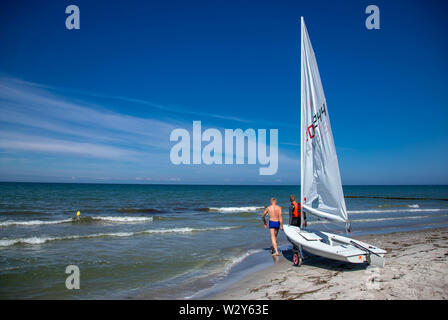 11 luglio 2019, Meclemburgo-Pomerania, Vitte: vacanzieri tirare una barca a vela da spiaggia sul Mar Baltico isola di Hiddensee nel Mar Baltico. Clima mite e sole attirano i turisti e ospiti alla costa. Foto: Jens Büttner/dpa-Zentralbild/ZB Foto Stock