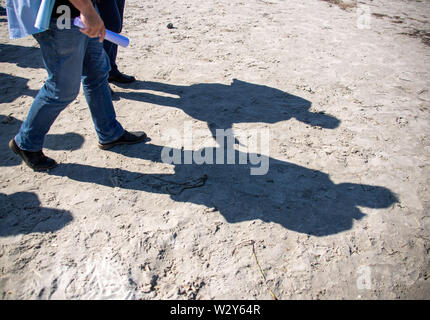 11 luglio 2019, Meclemburgo-Pomerania, Vitte: l'ombra del ministro dell' agricoltura di Mecklenburg-Vorpommern (sopra) e un accompagnatore può essere visto sulla spiaggia del Mar Baltico isola Hiddensee. Il ministro informa sul sito circa la nuova costruzione di groyne righe. Sulla costa fuori del villaggio di Vitte, un nuovo sistema groyne fu costruito per circa cinque milioni di euro per proteggere efficacemente i villaggi dalle forti mareggiate con un livello di piena fino a 2,60 metri. Foto: Jens Büttner/dpa-Zentralbild/dpa Foto Stock