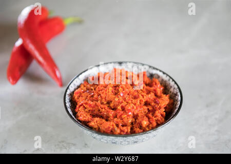 Magrebino tradizionale peperoncino piccante salsa Harissa su un marmo grigio Sfondo. Cucina Araba. Adjika di salsa al peperoncino piccante. Peperoncini calabrese con o Foto Stock