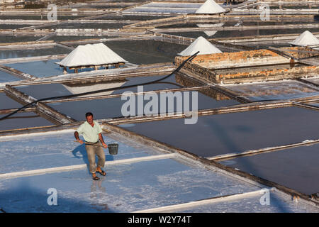 L uomo si diffonde acqua attraverso le saline di Rio Maior, Portogallo Foto Stock