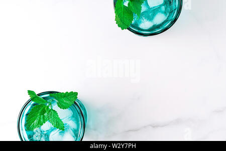 Due belle vintage occhiali turchese con bevanda fredda e cubetti di ghiaccio, decorata con fresco verde menta su marmo bianco tavola. Vista dall'alto. Foto Stock