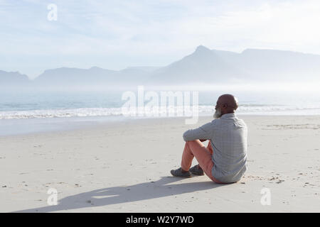 Uomo seduto sulla sabbia della spiaggia. Foto Stock