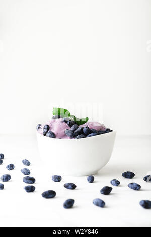 Ice-cream decorata con frutti di bosco freschi di caprifoglio e foglie verdi su sfondo bianco. Close-up. Foto Stock