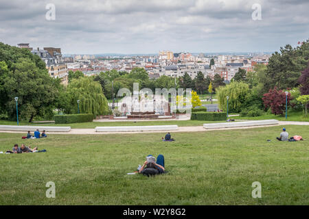 Parigi, Francia - 26 Maggio 2019: Butte du Chapeau Rouge park a Parigi con la gente il relax e la lettura sull'erba Foto Stock