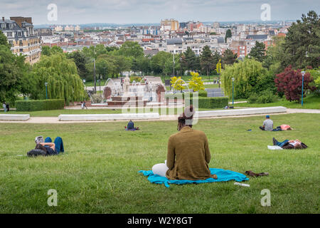 Parigi, Francia - 26 Maggio 2019: Butte du Chapeau Rouge park a Parigi con la gente il relax e la lettura sull'erba Foto Stock