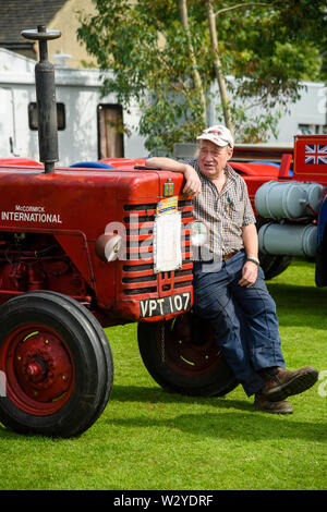 L'uomo (proprietario) seduti sulla ruota del 1956 International B250 Trattore, presentano parcheggiato sul display - Veicolo Classic show, Burley-In-Wharfedale, Inghilterra, Regno Unito. Foto Stock