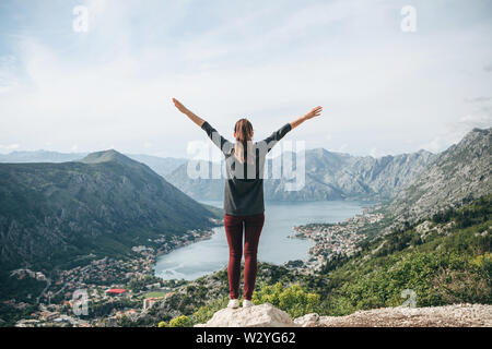 Vista posteriore bambina alza le mani in alto. Ammira la città di Kotor in Montenegro e mostra come felice che lei è. Foto Stock