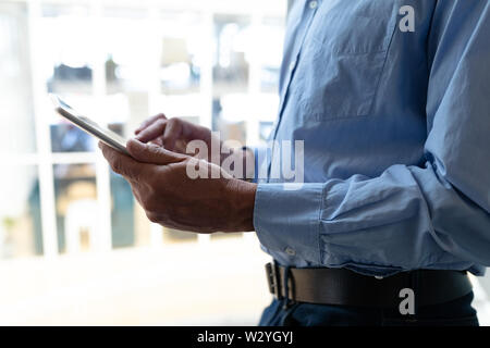 Imprenditore lavora su tavoletta digitale mentre in piedi vicino alla finestra in ufficio Foto Stock