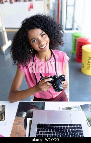 Femmina di graphic designer rivedendo le foto sulla fotocamera digitale a scrivania in ufficio Foto Stock