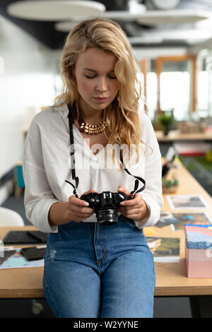 Femmina di graphic designer rivedendo le foto sulla fotocamera digitale in un ufficio moderno Foto Stock