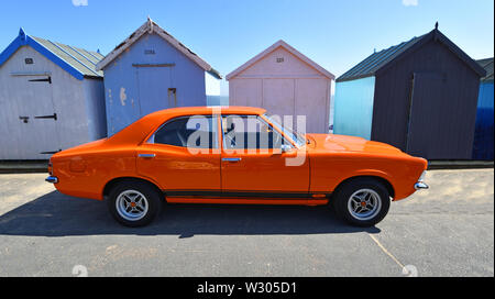 Arancione classico Ford Cortina MK3 auto parcheggiate davanti alla spiaggia di capanne. Foto Stock