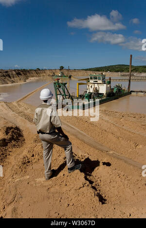 Gestione e trasporto di sabbie minerali di titanio. Estrazione mineraria da dragaggio in stagni di acqua dolce. Draghe che getti l'acqua sulla faccia di sabbia & sul supervisore sulla banca Foto Stock