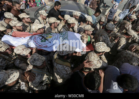 Jabalya, Territori palestinesi. 11 Luglio, 2019. I membri delle forze di sicurezza palestinesi di Hamas movimento islamista portano il corpo di Mahmoud al-Adham, 28, durante il suo funerale dopo aver ceduto alle sue ferite all'ospedale. L'esercito israeliano ha detto giovedì i suoi soldati sembravano aver scambiato un "Hamas ritenuta' operativa per un terrorista armato, che li conduce a fuoco aperto. Credito: Mohammed Talatene/dpa/Alamy Live News Foto Stock