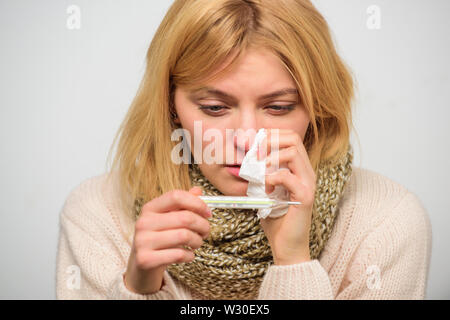 Prendere la temperatura e valutare i sintomi. Misurare la temperatura. La donna si sente male male starnuti. La ragazza di sciarpa tenere il termometro e il tessuto vicino. Freddo e rimedi influenza. Alta temperatura del concetto. Foto Stock