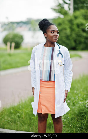 Giovane americano africano medico donna in camice bianco con uno stetoscopio poste all'esterno. Foto Stock