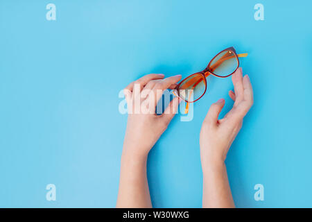 Mani femminili tenendo delicatamente i bicchieri con le punte delle dita su sfondo blu. Foto Stock