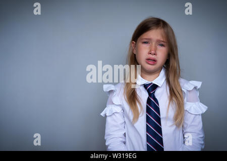 Piccolo schoolgirl ricopre la faccia, ritratto di pianto. Preteen ha sottolineato, spaventata bambino nascondere, asciugare le lacrime. Allievo, studente in uniforme scolastica. Torna a sc Foto Stock