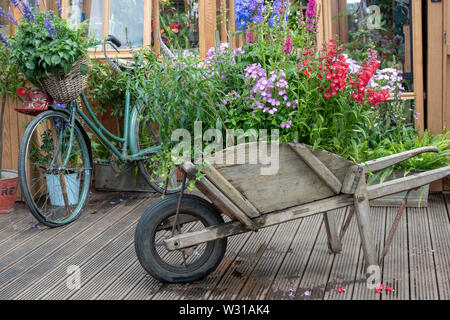 Vecchia carriola e bicicletta nella parte anteriore di una serra su un display ad RHS Hampton Court flower show 2019. Hampton Court, Surrey, Inghilterra Foto Stock