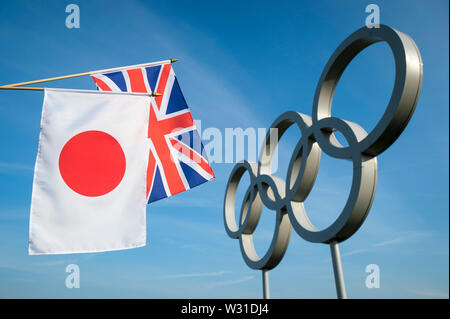 Londra - 19 Aprile 2019: Giapponese e Regno Unito Union Jack appendere bandiere insieme davanti ad un grande insieme di metallica lucida anelli olimpici sotto il luminoso cielo blu. Foto Stock