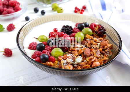 Yogurt, muesli, frutti di bosco freschi in un recipiente su un bianco sullo sfondo di legno. Delizioso e salutare prima colazione. Una corretta alimentazione. Menu dietetici. Foto Stock