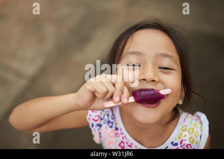 Ragazza asiatica a mangiare il gelato in all'aperto. Filipina kid mangiare un gelato e a fissare la fotocamera. Foto Stock