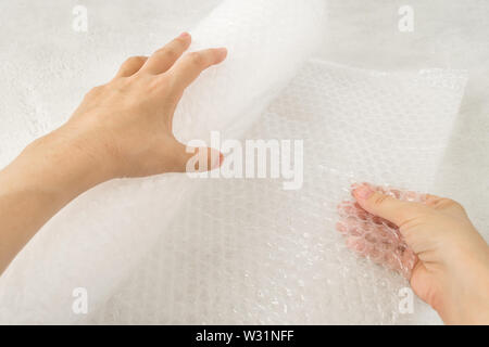 Donna mani tenere un rotolo di bianco trasparente Bubble wrap su una ruvida sfondo bianco. Materiale per l'imballaggio di oggetti fragili per un trasporto sicuro. Foto Stock