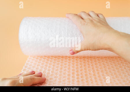 Donna mani di svolgere una bobina di bianco trasparente Bubble wrap su sfondo giallo. Materiale per l'imballaggio di oggetti fragili per un trasporto sicuro. Foto Stock