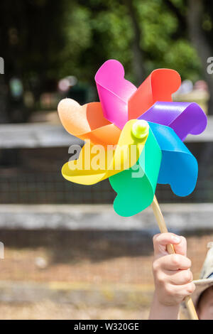 Una mano che tiene un bambino colorato milti rainbow mulino a vento Foto Stock