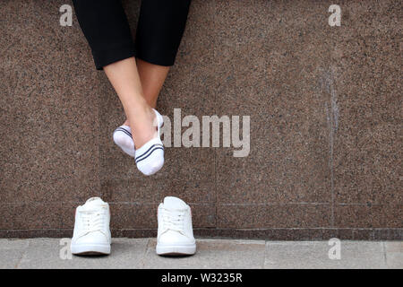 Gambe Stanche, donna a piedi nudi con rimosso white sneakers in appoggio su una strada. I piedi femminili in calze bianche, ragazza seduta e rilassante dopo aver eseguito Foto Stock