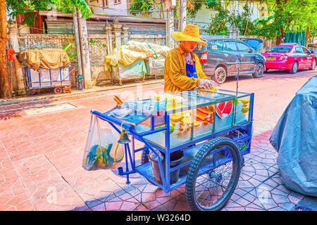 BANGKOK, Tailandia - 22 Aprile 2019: Il commerciante vende frutta fresca, ammassi di esse giacciono in ghiaccio nel bicchiere vetrina del suo carrello, su Aprile 22 in Ba Foto Stock