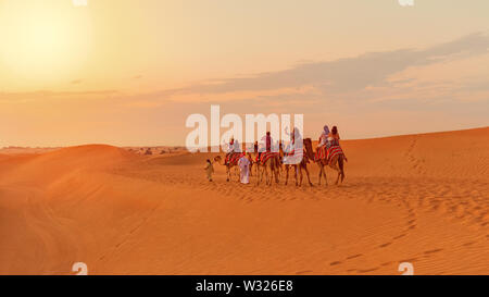 Safari nel Deserto i turisti a cavallo di cammelli sul caravan ad esplorare le dune di sabbia nel deserto di Dubai al tramonto Foto Stock