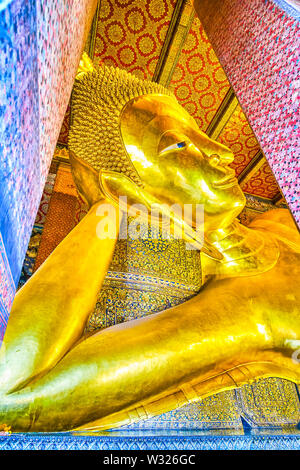 BANGKOK, Tailandia - 22 Aprile 2019: Il grande golden reclinabili Buddha Signore supporta la testa con il braccio attraverso le enormi colonne di Viharn Phranorn temp Foto Stock