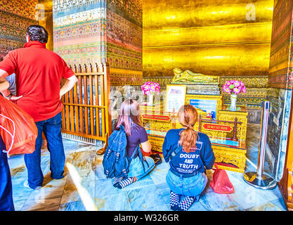 BANGKOK, Tailandia - 22 Aprile 2019: Due ragazze seduto sulle ginocchia e pregare presso il piccolo altare di Buddha reclinato in Viharn Phranorn santuario di Wat Pho te Foto Stock