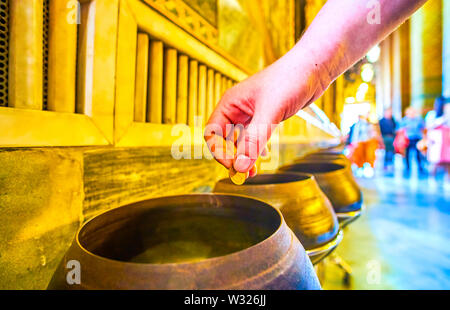 BANGKOK, Tailandia - 22 Aprile 2019: il rituale di far cadere la moneta in un vaso di bronzo, che possono portare una buona fortuna al Wat Pho tempio complessi su Ap Foto Stock