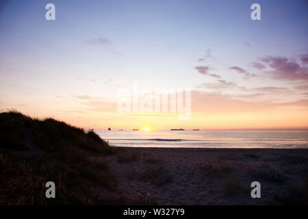 Alba sulla spiaggia prospiciente il traffico marittimo di navi mercantili caricati con contenitori. Foto Stock