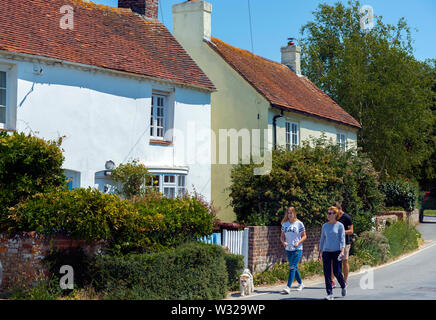 I turisti a piedi un cane nel villaggio sul mare di West Wittering su un giorno d'estate No. Chichester, West Sussex, in Inghilterra, Regno Unito Foto Stock